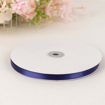 Navy blue satin ribbon on a spool against a plain background