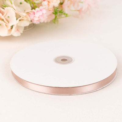 Rose gold satin ribbon on a spool against a soft background.
