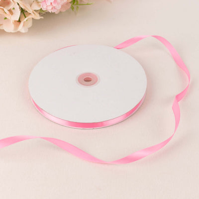 Pink satin ribbon on a spool with a delicate floral background.