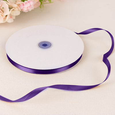 Purple satin ribbon spool with white ribbon on a soft floral background