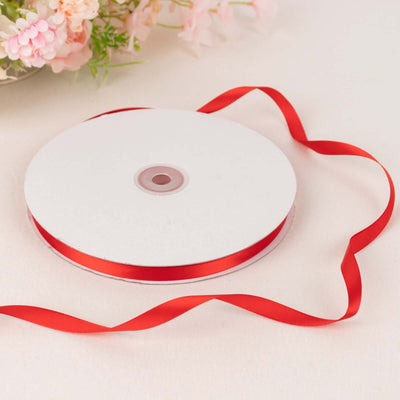Red satin ribbon on a spool with loose ribbon curls.