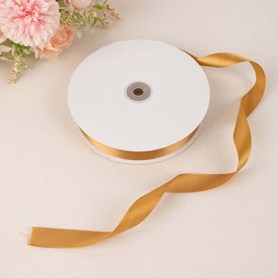 Gold satin ribbon spool on a soft background with floral accents.