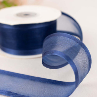 Navy blue sheer ribbon on a spool with a flowing curl.