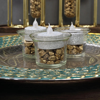 Sparkling candle holders with gold stones on a decorative plate.