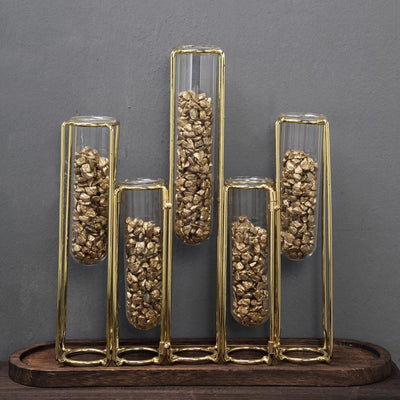 Gold and glass vase display with decorative stones on a wooden base.