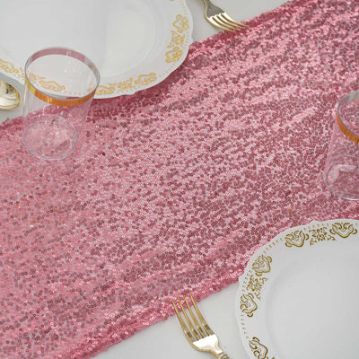 Pink sequin table runner on a white table with elegant dinnerware.