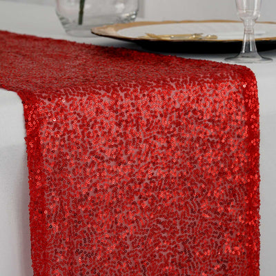Red sequin table runner on a dining table setting with elegant decor.