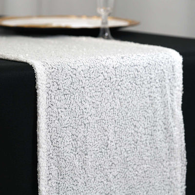 Elegant white sequin table runner on a dark table setting.