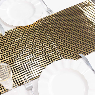 Gold grid table runner on a white table setting with plates and cutlery.