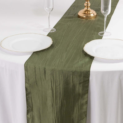 Olive green table runner on a white table with elegant plates and glasses.