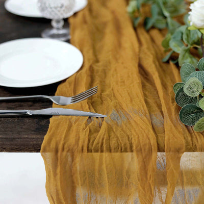Mustard yellow table runner on rustic wooden table with plates and greenery.
