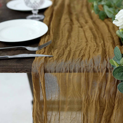 Wrinkled brown table runner on a rustic wooden table with plates and cutlery.