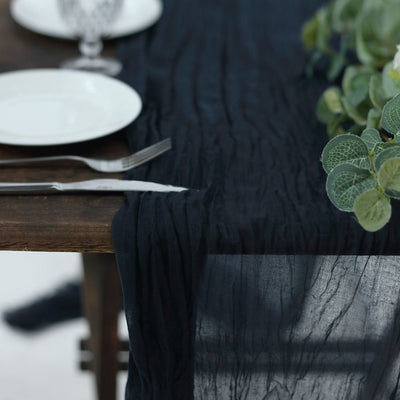 Black crinkled table runner draped over a wooden table with plates and greenery.