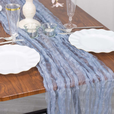 Elegant sheer blue table runner on wood dining table with white plates and glassware.