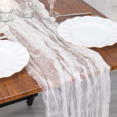 Sheer white table runner draped over a wooden table with plates and glasses.
