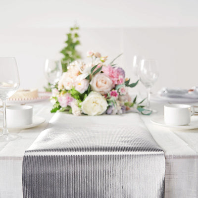Elegant silver table runner on a beautifully set dining table with flowers.