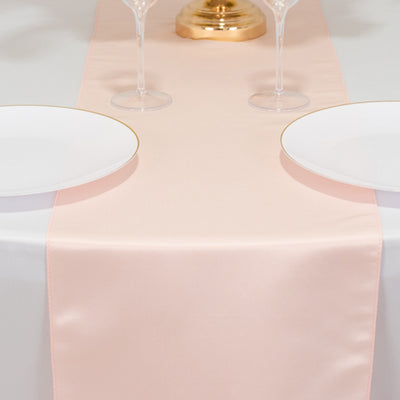 Elegant blush satin table runner on a dining table with white plates and glasses.