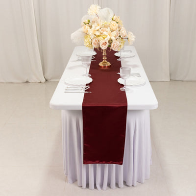 Elegant burgundy table runner on a white table set for dining with floral centerpiece.