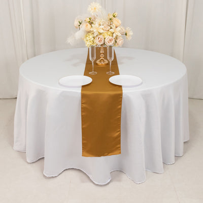 Round table set with white tablecloth, gold runner, plates, and floral centerpiece.
