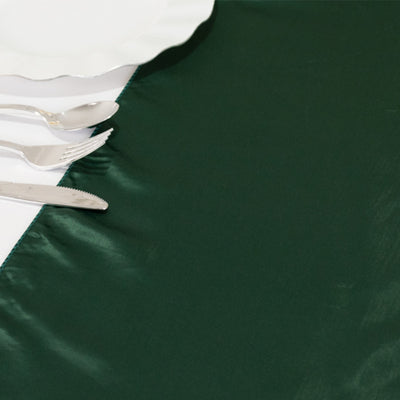 Green satin table runner on a white table setting with silver cutlery.