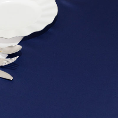 White scalloped plate with silver trim and stainless steel cutlery on a navy tablecloth.