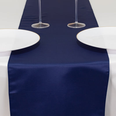 Navy satin table runner on a white table with plates and glasses.