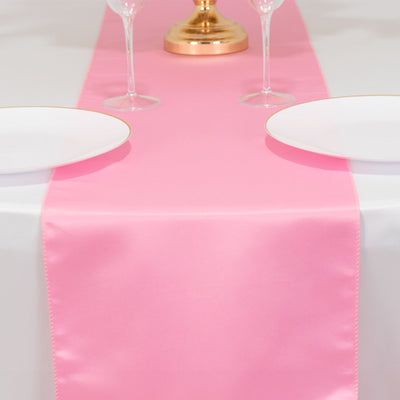 Pink satin table runner on a dining table with plates and glasses.