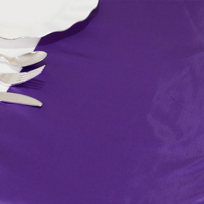 White dinner plate and silver cutlery on a purple tablecloth.