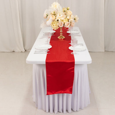 Red satin table runner on a white table with floral centerpiece and glassware.
