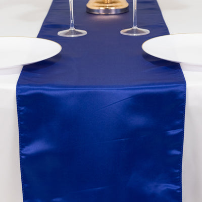 Navy blue satin table runner with plates and glasses on a white table.