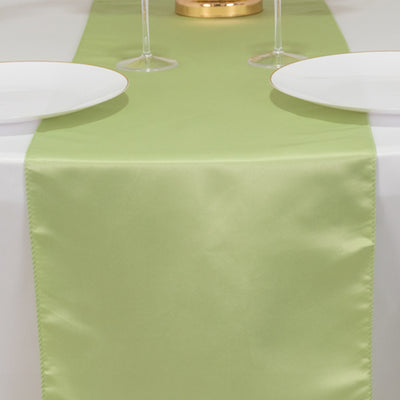 Green satin table runner on a white table with plates and glasses.