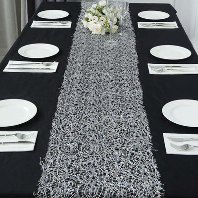 Elegant silver table runner on a black table with plates and floral centerpiece.