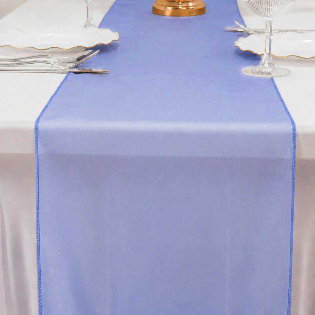 Blue sheer table runner on a white dining table with glassware and plates.