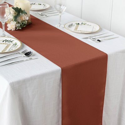 Brown table runner on elegantly set dining table with white and decorative plates.