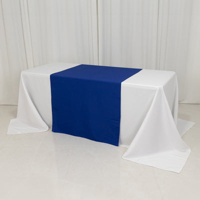 Table with white drapes and a blue runner, set against a plain backdrop.