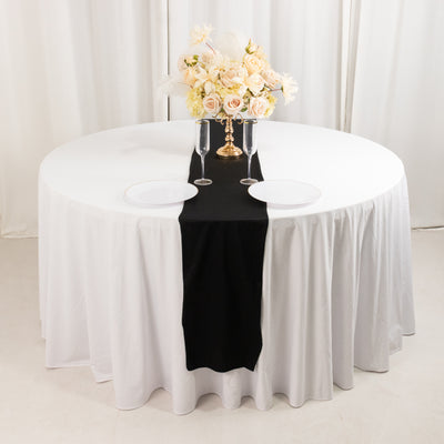 Elegant round table set with white and black tablecloth, floral centerpiece, and dinnerware.