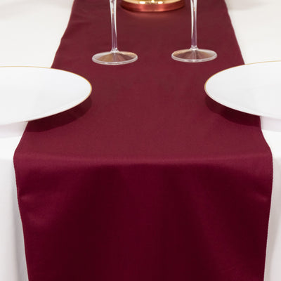 Burgundy table runner on a dining table with plates and wine glasses.