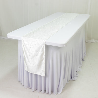 White table with a sparkling silver runner centered on a draped tablecloth.