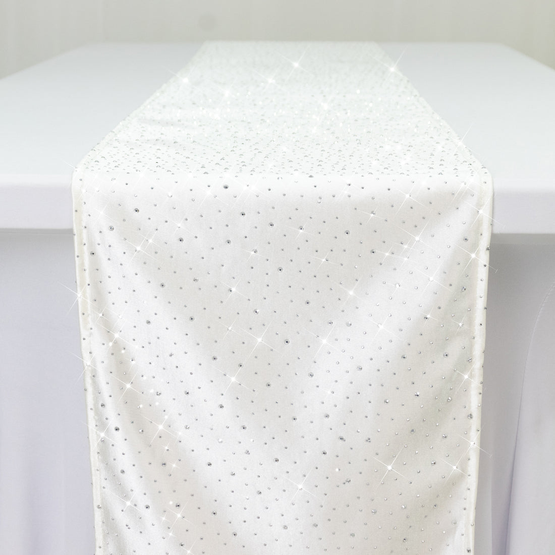 White table runner with sparkling rhinestones on a plain backdrop.