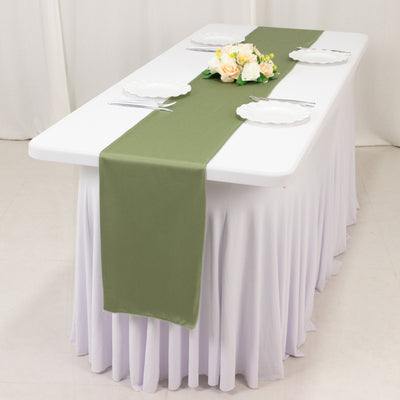 Olive green table runner on a white table with plates and floral centerpiece.