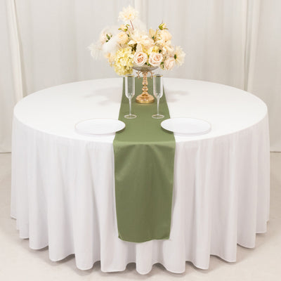 Elegant round table set with white tablecloth, green runner, plates, and floral centerpiece.