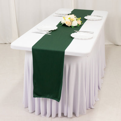 Green table runner on a white table set with plates and flowers.