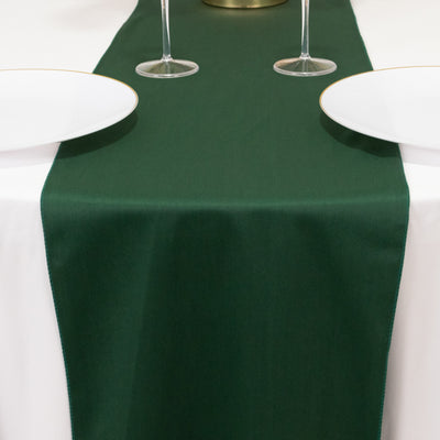 Green table runner on a set dining table with plates and glasses.