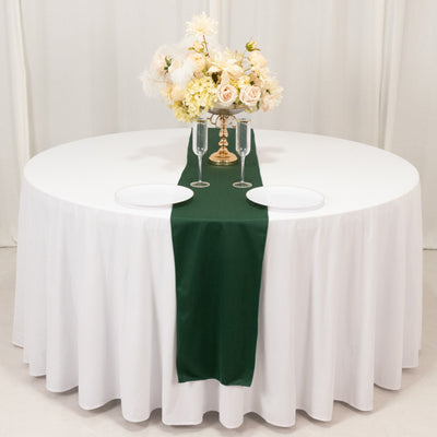 Elegant round table set with white tablecloth, green runner, and floral centerpiece.