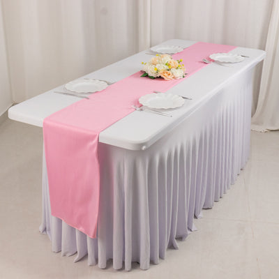 Pink table runner on a white table set for dining with plates and floral centerpiece.