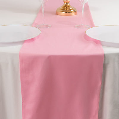 Pink table runner on a dining table with plates and a centerpiece.