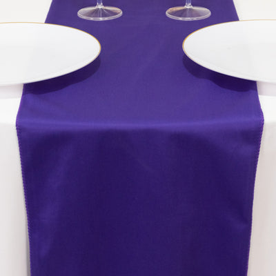 Purple table runner with two white plates and glasses on a dining table.