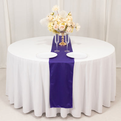 Round table set with white tablecloth, purple runner, and floral centerpiece.