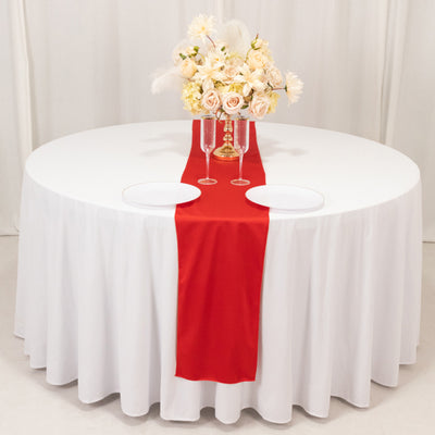 Elegant round table set with red runner and floral centerpiece.