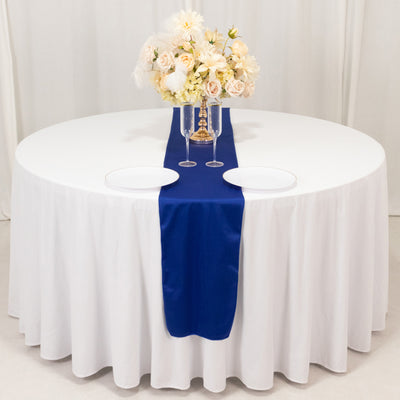 Elegant round table set with white tablecloth, blue runner, and floral centerpiece.